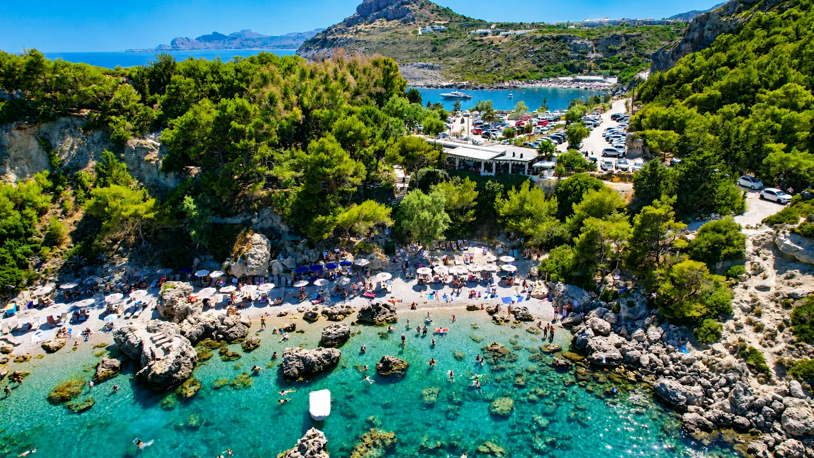 Close aerial view of Anthony Quinn Bay with turquoise water and rocky shore